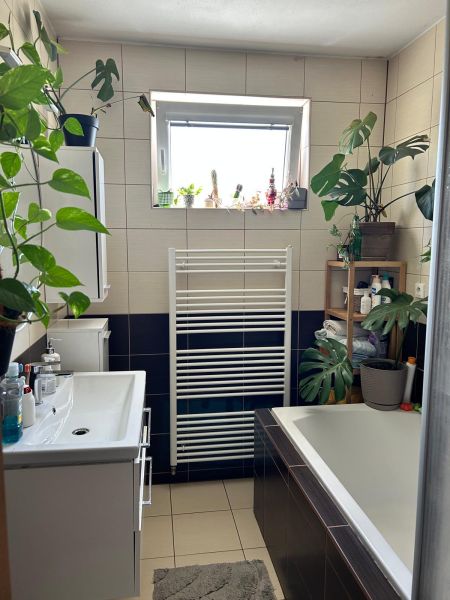 Háromszobás lakás fürdőszobája káddal, növényekkel és kis ablakkal.
