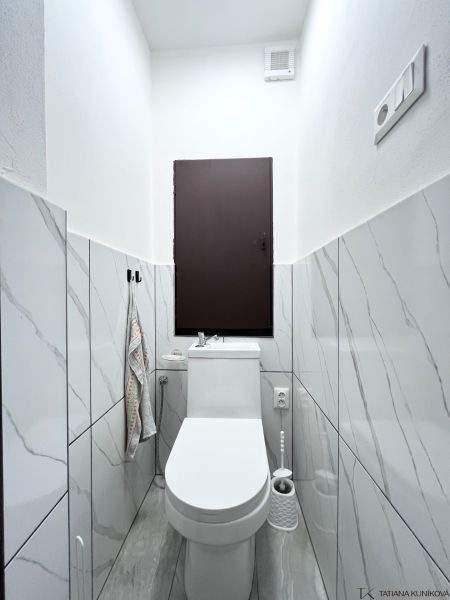 WC egy 3 szobás lakásban márvány burkolattal és fehér szaniterekkel.