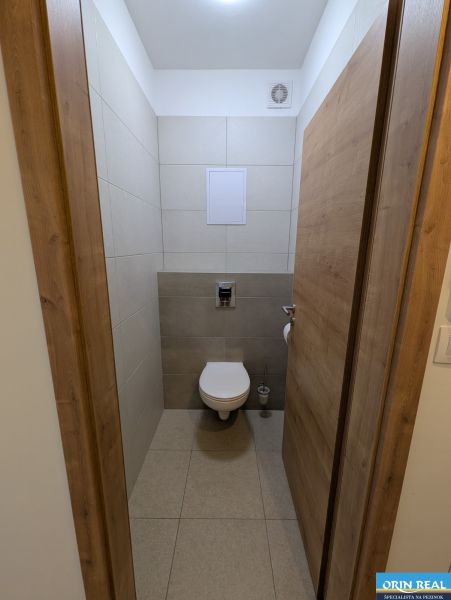 Kétszobás lakás fürdőszobája kerámia burkolattal és fa hatású padlóval.