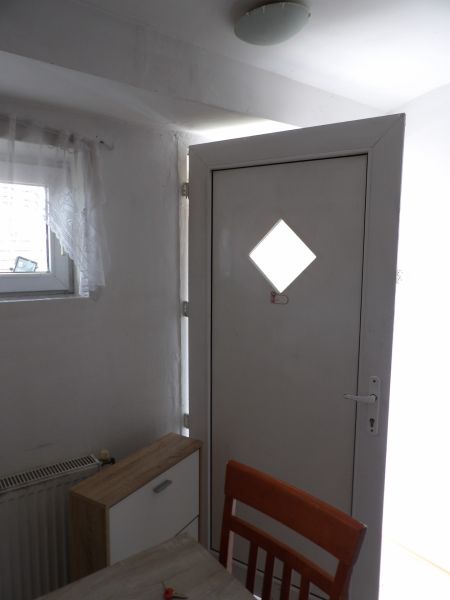Bejárati ajtó egy kétszobás lakásban fa dekorációjú komóddal és székkel.