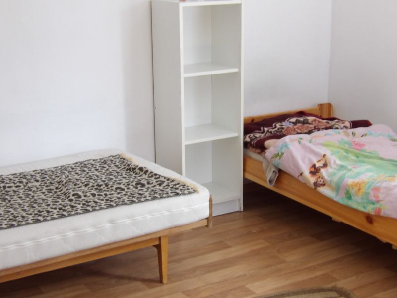 Két ágy, polc és fa dekorációjú padló egy kétszobás lakásban.