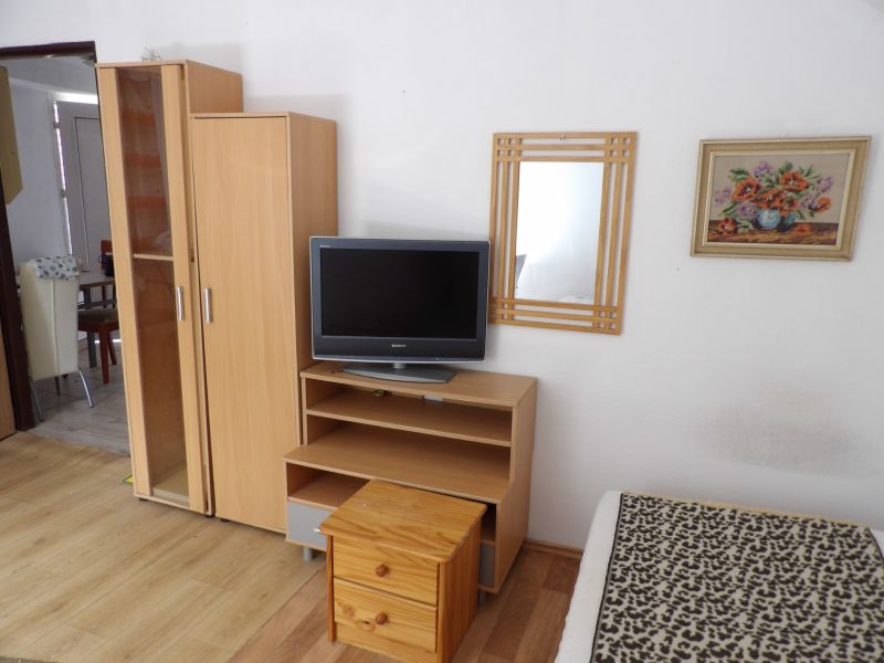 Televízió alacsony szekrényen, szekrény és tükör egy kétszobás lakásban, fa dekor padlóval.