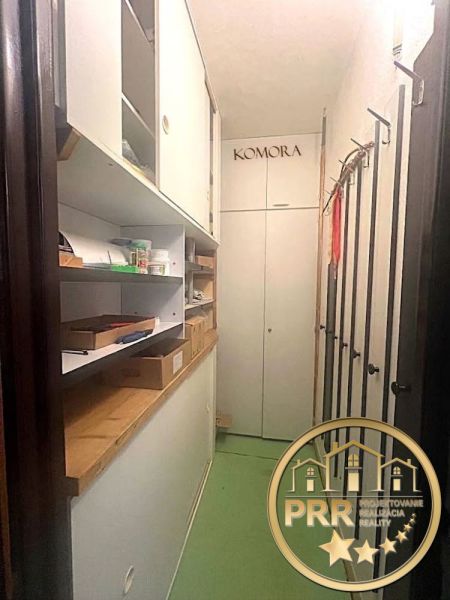 Tárolóhely egy kétszobás lakásban polcokkal és dobozokkal, zöld padlóval.