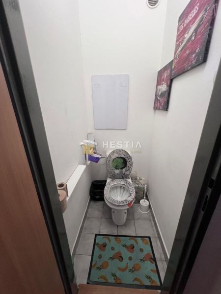 Két szobás lakás WC-je mintás szőnyeggel és fali dekorációval.