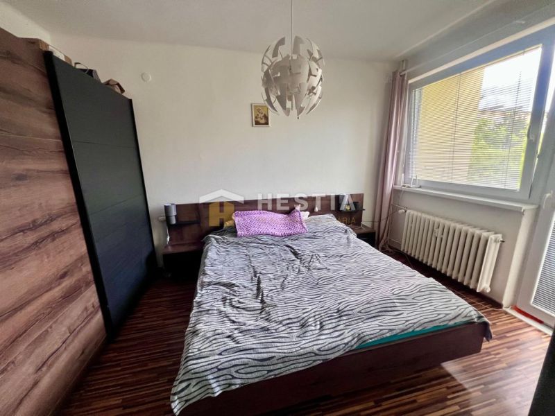 Hálószoba egy kétszobás lakásban fa mintázatú padlóval és nagy ablakkal.