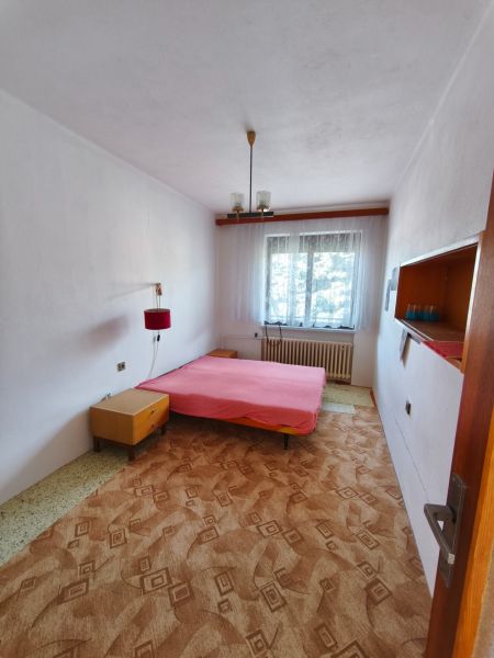 Hálószoba családi házban ággyal, szőnyeggel és fehér függönyös ablakkal.