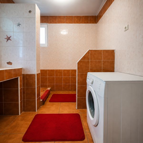 Fürdőszoba családi házban zuhanyzóval és mosógéppel, barna árnyalatú csempével.