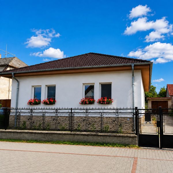 Családi ház Sellyén fehér homlokzattal, ablakvirágokkal és kontyolt tetővel.