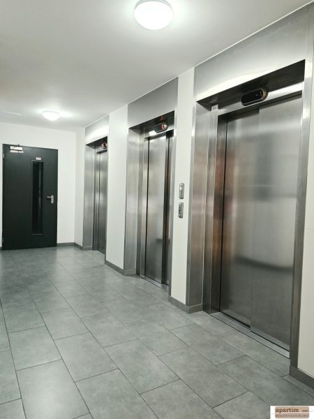 Egy négy szobás lakás folyosója négy fém lifttel és szürke csempével.