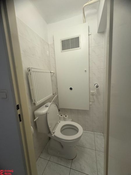 Fürdőszoba egy egyszobás lakásban WC-vel, világos csempékkel és radiátorral.