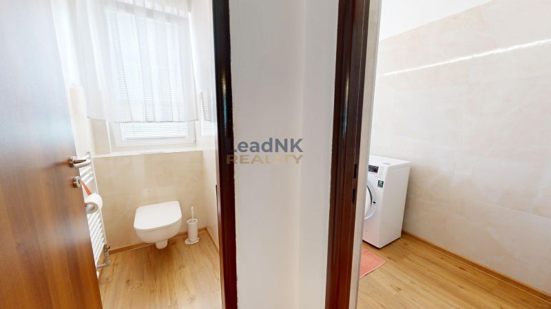 Fürdőszoba egy háromszobás lakásban WC-vel, mosógéppel és fa dekoros padlóval.