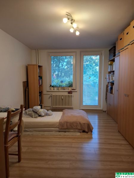 Szoba egy háromszobás lakásban ággyal, polcokkal és fa dekorációjú padlóval.