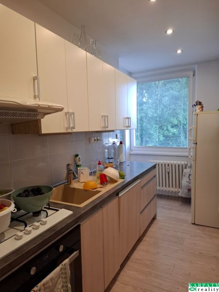 Konyha egy háromszobás lakásban, fa dekorációjú padlóval és világos szekrényekkel.