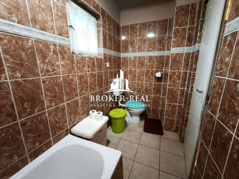 Fürdőszoba barna csempékkel, káddal, WC-vel és szemetes edénnyel egy családi házban.