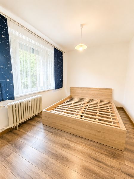 Hálószoba fa mintázatú padlóval és ággyal egy háromszobás lakásban.