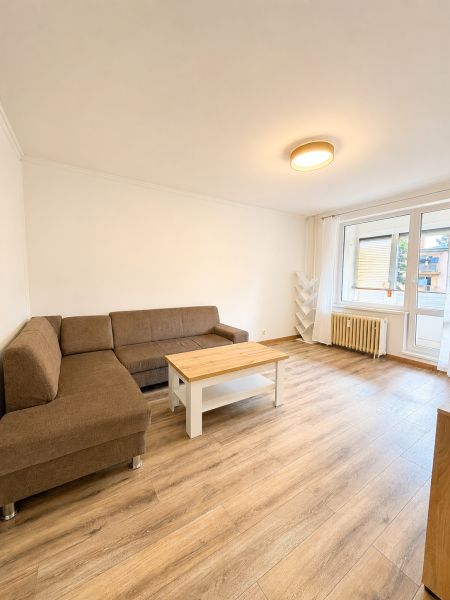 Nappali egy háromszobás lakásban kanapéval, dohányzóasztallal és fa dekorációjú padlóval.