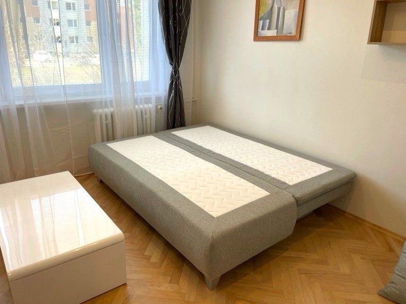 Garzonlakás ággyal, fa mintázatú padlóval és fehér asztallal.