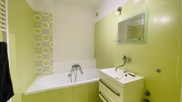 Zöld-fehér fürdőszoba káddal és mosdóval egy háromszobás lakásban.