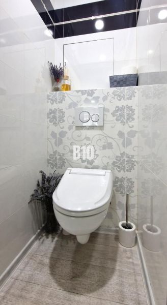 Egyszerűen berendezett WC dekoratív csempékkel és fa mintázatú padlóval.