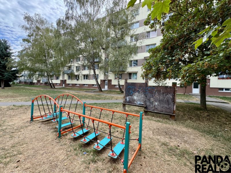 Egy lakóház külseje Topoľčanyban játszótérrel és növényzettel az egyszobás lakás körül.