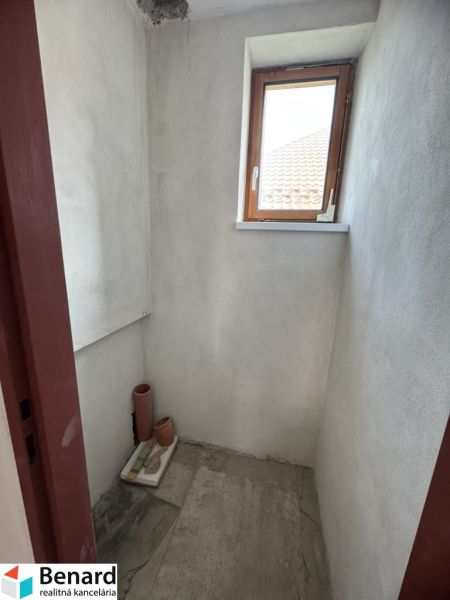 Kis szoba ablakkal egy családi házban, festetlen falak, csempe a padlón.