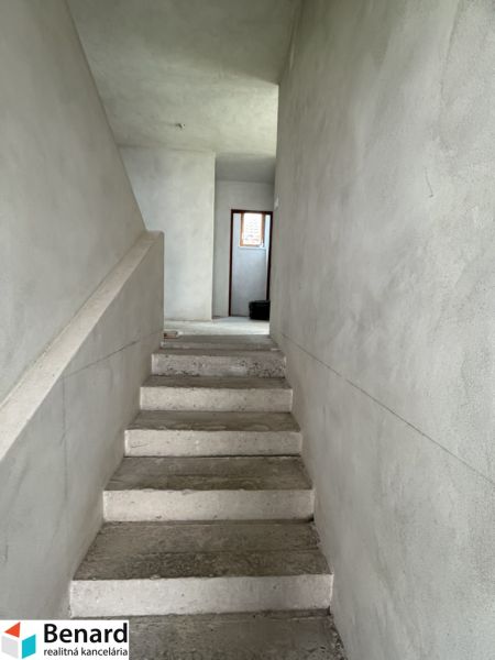 Betonlépcsők vezetnek az emeletre egy családi házban vakolt falakkal.
