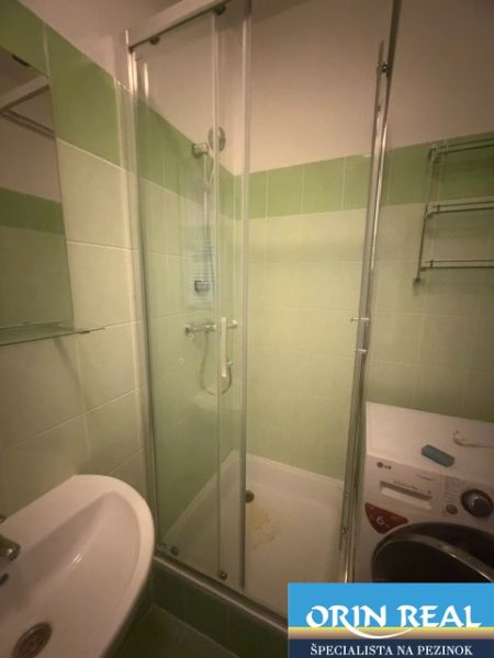 Fürdőszoba a garzonlakásban zuhanyzóval, mosógéppel és mosdókagylóval, kerámia burkolattal.