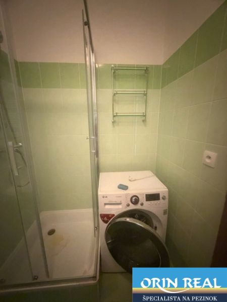 Fürdőszoba garzonlakásban zuhanyzóval és mosógéppel, zöld csempékkel.