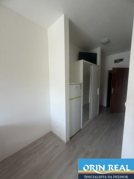 Garzonlakás fa dekor padlóval, hűtőszekrénnyel és beépített szekrénnyel.
