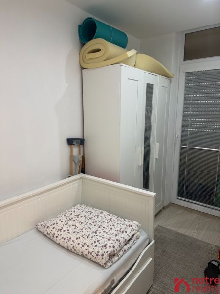 Szoba ággyal, szekrénnyel és feltekert matracokkal egy kétszobás lakásban.