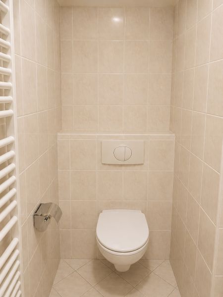 Fürdőszobai WC egy kétszobás lakásban, csempével és fali öblítőrendszerrel.
