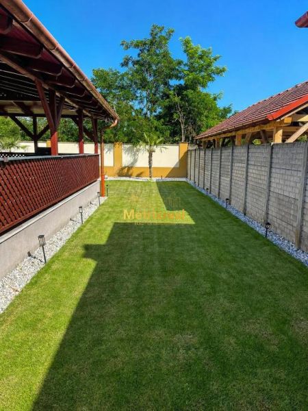 A családi ház kertje Darnózseliben gyepes, pergolával és fákkal körülvéve.