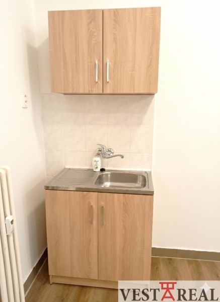 Kis konyhapult mosogatóval és szekrényekkel, fa dekoros padlóval.