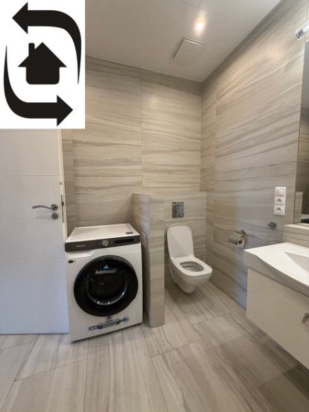 Fürdőszoba mosógéppel és WC-vel egy háromszobás lakásban, kőmintás csempékkel.