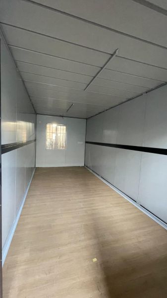 Egy fahatású padlóval, fehér falakkal és kis ablakkal rendelkező házikó belső tere.