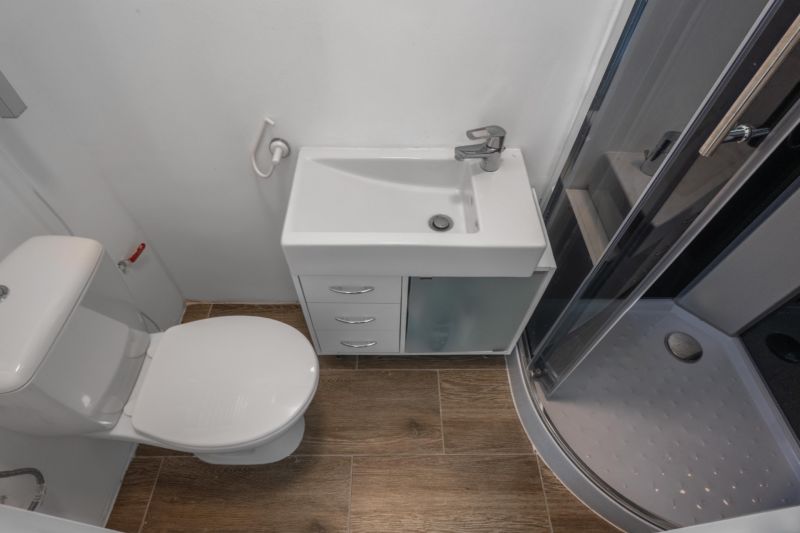 A fürdőszoba zuhanyzót, mosdót és WC-t tartalmaz, padlója fa dekorációval van ellátva.