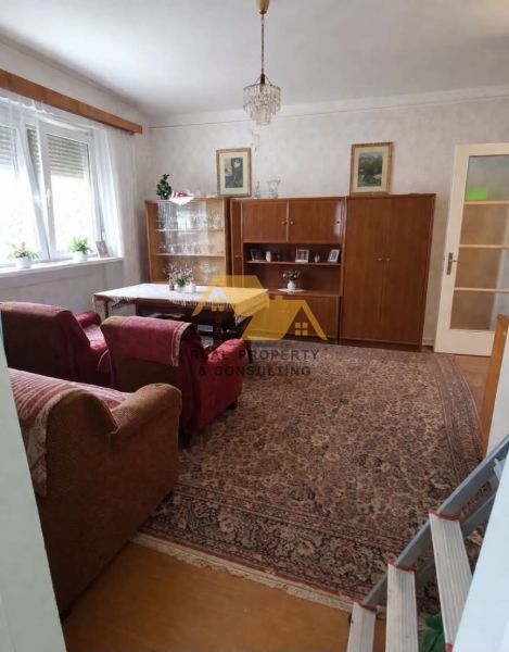 Nappali egy családi házban kanapéval, szekrénnyel és csillárral, fa dekorációjú padlóval.
