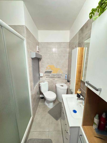 Fürdőszoba WC-vel egy egyszobás lakásban, csempékkel és zuhanyzóval.