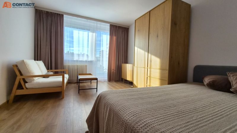 Szoba nagy ablakkal, kanapéval, ággyal, szekrénnyel és fa dekoros padlóval egy egyszobás lakásban.