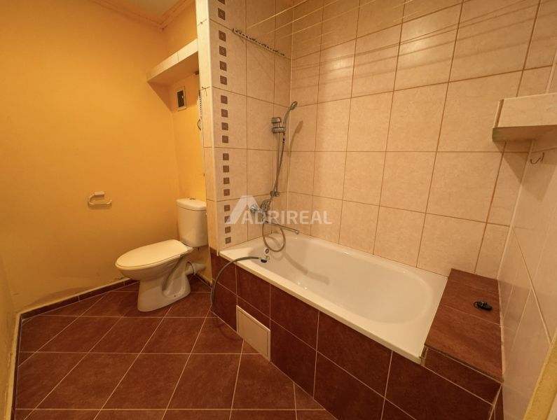 Fürdőszoba egy egyszobás lakásban káddal és WC-vel, barna tónusú csempékkel.