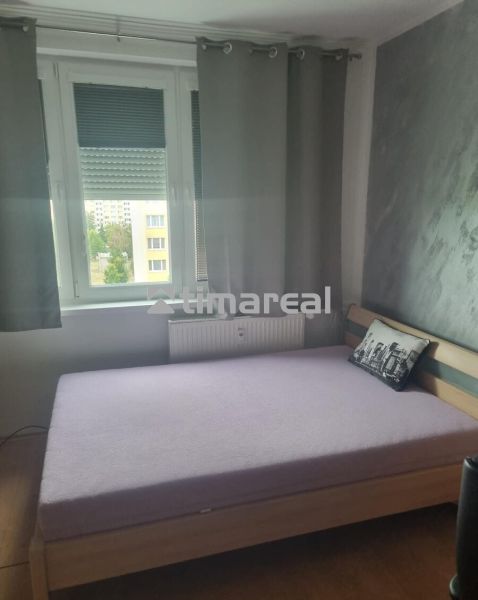 Hálószoba egy háromszobás lakásban ággyal és szürke dekoratív párnával.