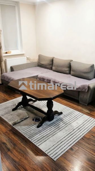 Nappali egy háromszobás lakásban kanapéval, asztallal, fa dekorációjú padlóval és szőnyeggel.