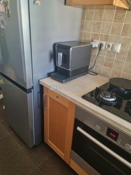 Konyha egy háromszobás lakásban hűtőszekrénnyel, tűzhellyel és kávéfőzővel a kőpulton.