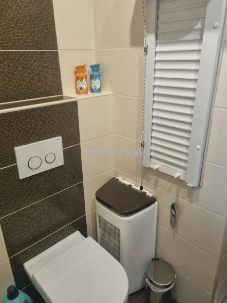Fürdőszoba WC-vel egy háromszobás lakásban, krém-barna csempe és tárolóhely.