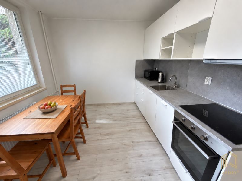 Konyha egy kétszobás lakásban fehér konyhabútorral és fa mintázatú padlóval.