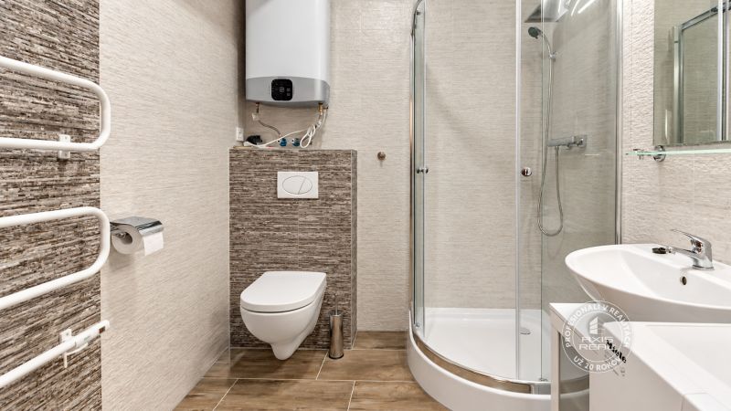 Fürdőszoba egy kétszobás lakásban, zuhanyzó, mosdó és WC-csésze fa dekorációjú padlóval.