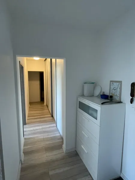 Folyosó egy kétszobás lakásban fehér komóddal és fa mintázatú padlóval.