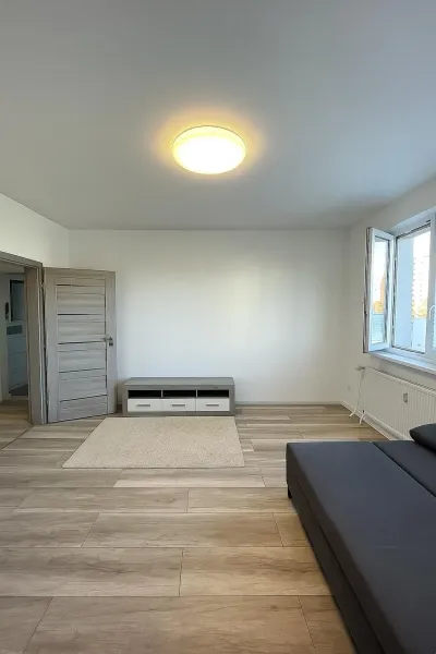 Világos nappali egy kétszobás lakásban, fa hatású padlóval és szürke kanapéval.
