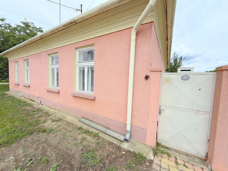 Családi ház Dunakilitiben rózsaszín homlokzattal, fehér ablakokkal és kapuval.