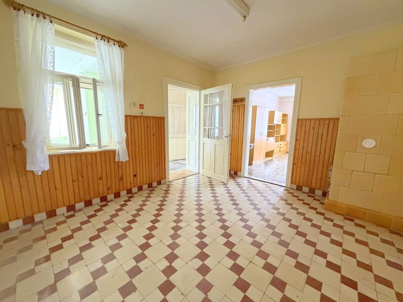 Családi ház belső tere, világos helyiség csempézett padlóval és fa burkolatú falakkal.